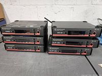 Six Sennheiser True Diversity Receivers EM 100 units arranged on a table with visible labels HAND, OVER-EAR, and CLIP-ON. One antenna is damaged.