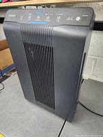 Black Winx air purifier standing on floor showing front vent and top control panel area.