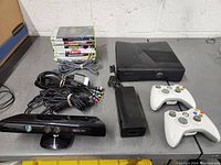 Full lot contents including Xbox 360 console, Kinect sensor, two wireless controllers, power supply, component cables, and stacked 7 game cases.