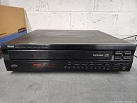 Front and top view of Yamaha CD player on a surface with cardboard in background showing power on and condition of unit.