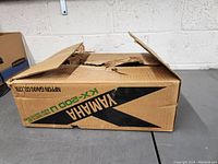 Closed cardboard box with 'Yamaha KX-200U' branding and markings, box is slightly torn and worn.