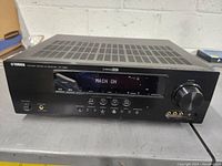 Front view of Yamaha RX-V665 receiver powered on, displaying 'MAIN ON' on the LCD display. Shows overall condition and front panel layout.