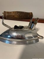 Side view of the vintage antique iron showing shiny metal body and wooden handle with signs of rust.