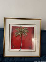 Framed print of a palm tree titled 'Princess Palm' against a red background with white mat and gold frame.