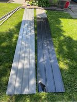 Two aluminum soffit panels lying on grass; a black vented panel and a putty unvented panel, showing length and color.
