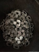 Photo showing a bucket filled with multiple metal framing H clips, piled inside a small container.