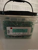 Plastic bucket container labeled with product details: Plastic Cap Nail, 2-1/2 inch (12 gauge), 1200 pcs, made in Canada.