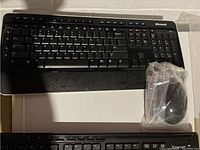 Microsoft wireless keyboard and black wireless mouse in plastic bag on white surface.