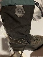 Side view of black SOREL insulated winter boot showing fabric and rubber construction with SOREL logo patch.