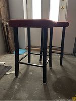 Side view of two bar stools with black metal legs and red padded seats in dark garage floor area.