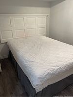 Photo showing white quilted mattress on double bed frame with paneled white wooden headboard.
