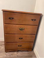 Front view of four-drawer maple dresser with metal handles showing scratches on wood surface.