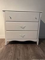 Front view of white painted dresser with three drawers, showing the design and drawer handles.