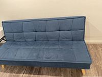 Front view of blue fabric futon couch bed with tufted cushions and wooden legs.