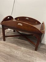 Side view of wooden coffee table showing the folding tray top with handle cutouts and sturdy legs with cross supports.