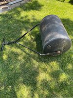 Full view of poly lawn roller lying on grass showing cylindrical roller and metal handle.