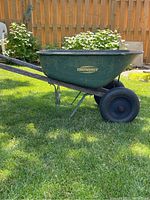 Side view of YardWorks two-wheeled garden wheelbarrow showing green metal basin and black rubber wheels on green frame.