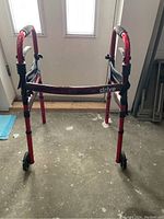 Front view of the red folding wheeled walker, showing its structure and two front wheels.