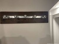 Photo shows a wall-mounted coat rack with a dark wood base and five metal hooks attached horizontally to a wall.