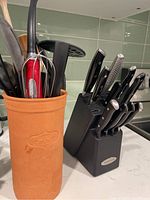 Black knife block with various knives and terracotta utensil holder with kitchen tools