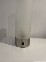 Photo of the table lamp powered off showing the cylindrical frosted glass shade and brushed metal base with a switch.
