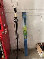Photo of black wrought iron floor lamp standing next to red toolbox, shows lamp base, stand and socket.