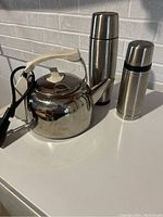 Photo shows a stainless steel Russell Hobbs electric kettle with cream handle and two stainless steel thermos bottles of different sizes.