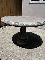 Front view of the round concrete patio table showing the decorative pattern on the edge and the overall shape.