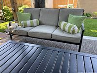 Three-seat loveseat with grey cushions, green square and striped bolster pillows