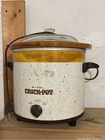 Vintage Rival Crock-Pot slow cooker with yellow band, dial, and glass lid. Shows signs of age and use.