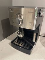 Front angle view showing stainless steel panel, control knob, indicator lights, portafilter, and drip tray.