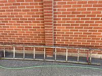 Full view of the wooden ladder lying on the ground against a brick wall, showing length and number of rungs.