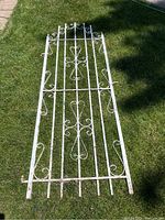 Full view of the white painted wrought iron gate or trellis with decorative scrollwork, displayed on grass.