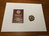2nd Class Order of the Patriotic War medal and its award certificate booklet displayed side-by-side on a flat white surface.
