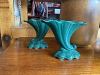 Pair of green pottery cornucopia vases on a wooden surface, showing overall shape and color.