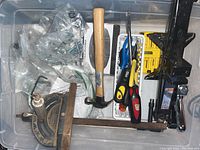 Box containing various hand tools such as hammers, screwdrivers, clamp, measuring square, and small hardware parts