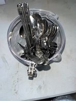 Top view of assorted silverware including spoons, forks, and butter knives inside a clear plastic container