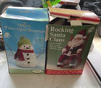 Photo showing original boxes of Hallmark Fiber-Optic Snowman and Rocking Santa Claus decorations placed on a flat surface.
