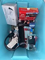 Blue plastic container filled with various boxed and loose items such as icicle lights, microphone set, phone case, and accessories.