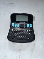 Front view of Dymo Label Manager 210d showing keyboard, display screen, and function buttons on a white surface.