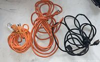 Photo of three extension cords: two orange and one black, coiled and laid out on a light surface.