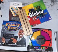 Photo showing Family Feud Platinum Edition, Blokus, Mancala Classic, iMatch Memory Game, and a wooden Cribbage board