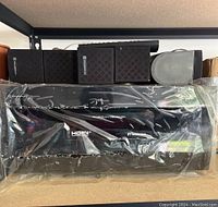 Front view of KraigerHiFi R-N303 receiver enclosed in plastic wrap with five black surround speakers stacked on top and beside it.