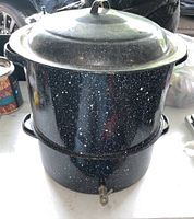 Full view of black enamel on steel 2-tier steamer pot with lid and spigot at base.