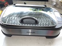 Front view of PowerXL smokeless indoor grill showing stainless steel sides, glass lid with handle, and grill surface.
