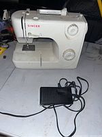 Full view of white Singer sewing machine with two dials and foot pedal corded.