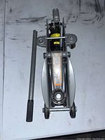 Top-down view of hydraulic car jack on a white surface showing the handle placed adjacent to the main body of the jack.