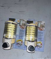 Two Depend brand soap dispensers in original packaging attached to cardboard with product info, cream colored with clear ribbed window and black dispensing button