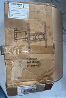 Closed damaged cardboard box with label describing the wall mount model and TV compatibility.