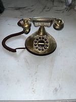 Front view of vintage brass rotary style telephone showing dial, handset and cord.